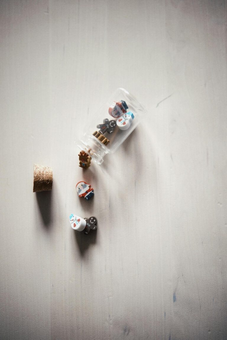 Tiny animal figures spill from a glass bottle on a minimalist surface, creating a playful scene.